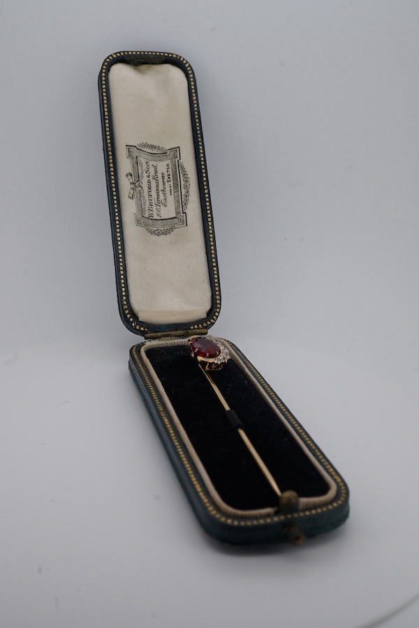 An early to mid 20th century yellow metal and single stone garnet topped doublet set stick pin, with diamond set crescent border, 61mm, gross weight 2.9 grams. Condition - fair to good